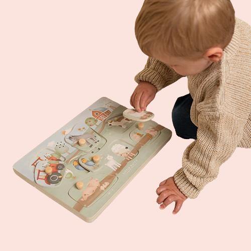 Mazulis spēlējas ar Little Dutch koka puzli “Little Farm” uz paklāja